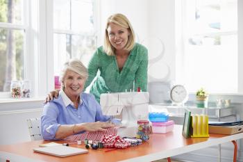 Senior Mother And Adult Daughter Use Sewing Machine At Home