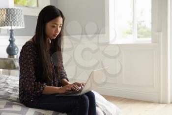 Woman Sitting On Bed In Bedroom Using Laptop Computer