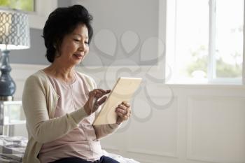 Senior Woman Sitting On Bed Using Digital Tablet