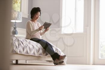 Senior Woman Sitting On Bed Looking At Photo Frame