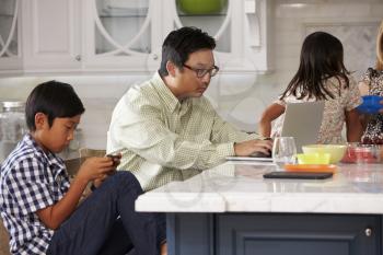 Family In Kitchen Having Breakfast And Using Digital Devices