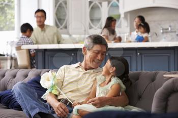 Grandfather And Granddaughter Relaxing On Sofa At Home