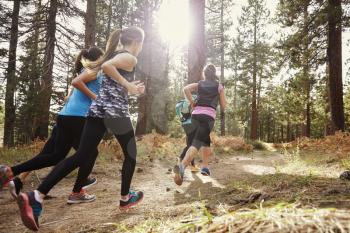 Group of young adult women running in a forest, back view