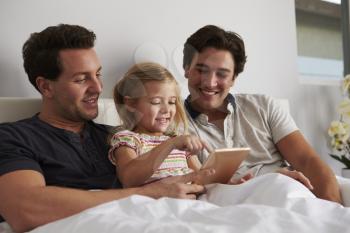 Daughter using digital tablet in bed with her male parents