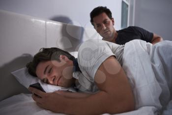 Man awake in bed, while his boyfriend secretly uses phone