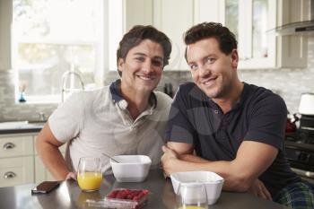 Male gay couple having breakfast in kitchen look to camera