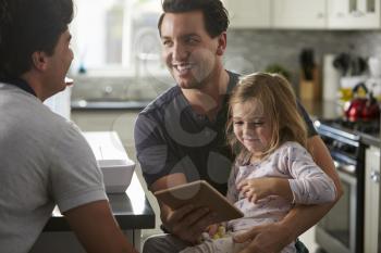 Male gay dads using tablet with daughter look at each other
