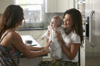 Female couple sitting in the kitchen holding their baby girl