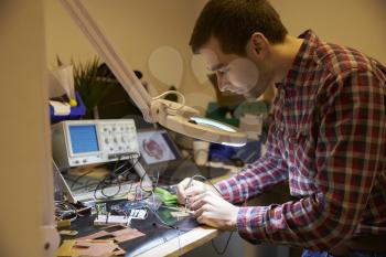 Electrical Engineer Soldering Circuit Board At Work Bench