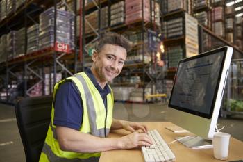 Man at computer in on-site warehouse office looks to camera