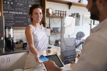Customer at coffee shop pays smiling waitress with card