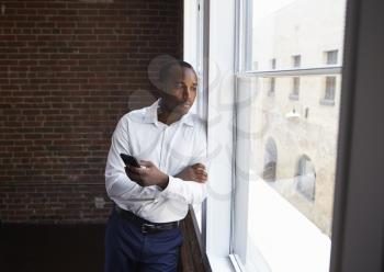 Businessman Checking Phone Standing By Office Window