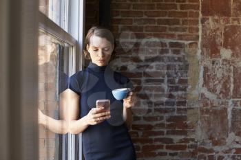 Businesswoman Checking Phone Standing By Office Window