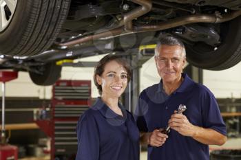 Male And Female Mechanics Working Underneath Car Together