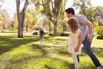 Father With Children Throwing Frisbee In Park Together