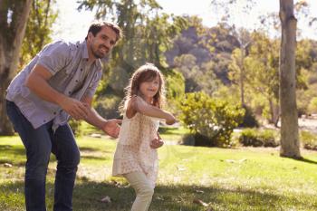 Father Teaching Daughter To Throw Frisbee In Park