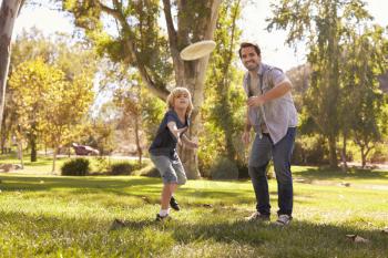 Father Teaching Son To Throw Frisbee In Park
