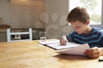 Boy Doing Homework Sitting At Kitchen Table