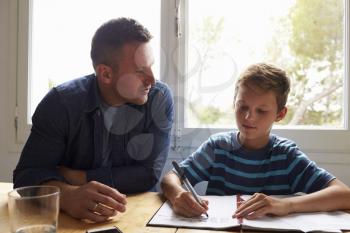Father Helping Son With Homework Sitting At Kitchen Table