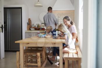 Kids do homework at kitchen table with mum while dad cooks