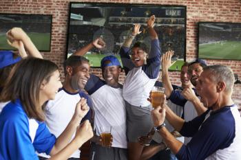 Friends Watching Game In Sports Bar On Screens Celebrating