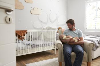 Father Sitting In Nursery Chair Holds Sleeping Baby Son
