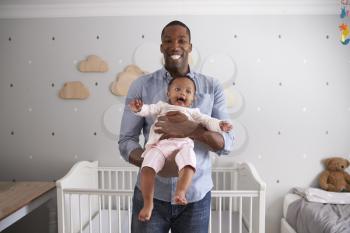 Portrait Of Father Holding Baby Daughter In Nursery