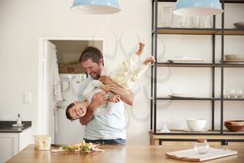 Father Playing With Son As They Prepare Food In Kitchen