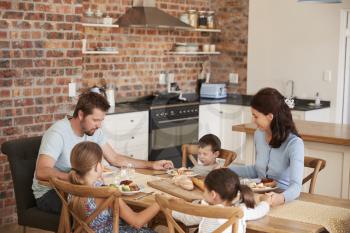 Family Praying Before Eating Meal In Kitchen Together