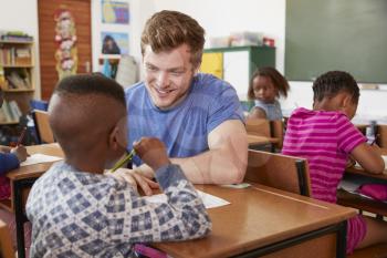White male teacher helping elementary school boy in class