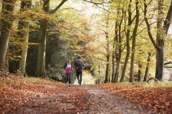 Mature Couple Running Through Autumn Woodland Together