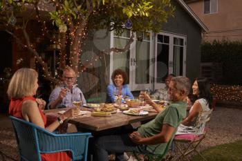 Group Of Mature Friends Enjoying Outdoor Meal In Backyard