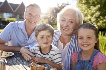 Portrait Of Grandparents With Grandchildren Enjoying Outdoor Summer Snack At Cafe
