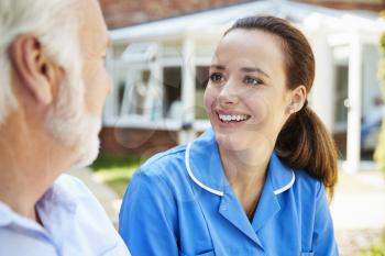 Senior Man Sitting On Bench And Talking With Nurse In Retirement Home