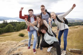 A group of five happy young adult friends cheer at the summit during mountain hike