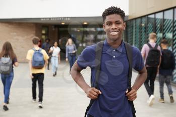 Portrait Of Smiling Male High School Student Outside College Building With Other Teenage Students In Background