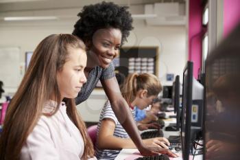 Teacher Helping Female Pupil Line Of High School Students Working at Screens In Computer Class