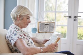 Senior woman sitting in an armchair reading a book at home