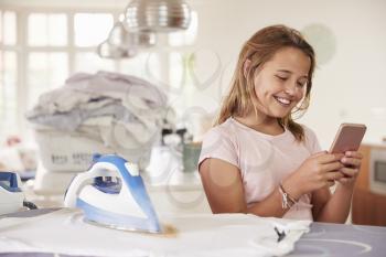 Young girl using distracted by phone while ironing