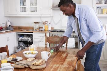 Man Clearing Breakfast Table And Loading Dishwasher