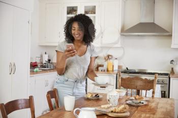 Teenage Girl Clearing Breakfast Table And Checking Mobile Phone