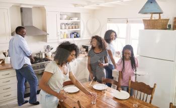 Family With Teenage Daughters Laying Table For Meal In Kitchen
