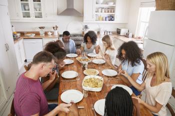 Two Families Saying Grace Before Eating Meal Together