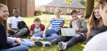 Teenage Students Sitting Outdoors And Working On Project