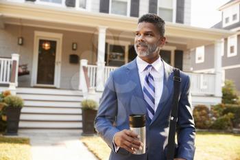Businessman With Cup Of Coffee Leaving Suburban House For Work