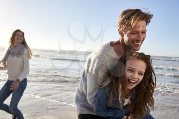 Parents With Daughter Having Fun On Winter Beach Together
