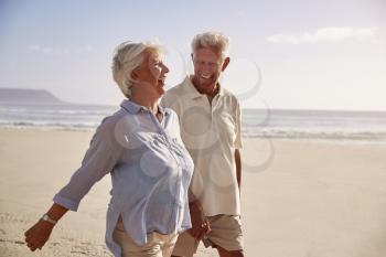 Senior Retired Couple Walking Along Beach Hand In Hand Together