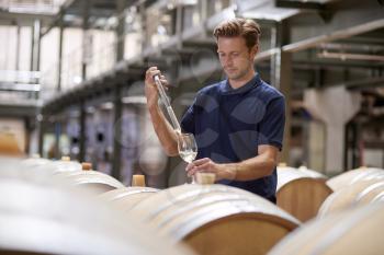 Young man testing wine in a wine factory warehouse