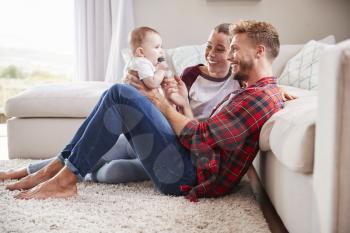 Young white couple play with their toddler in sitting room
