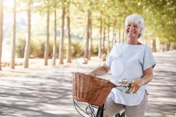 Portrait Of Smiling Senior Woman Cycling On Country Road